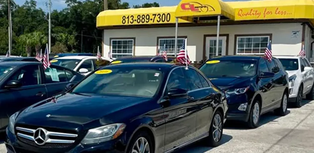 Exterior shot of the C&L Motors car dealership featuring a line of vehicles in front of a building with a yellow awning and American flags.